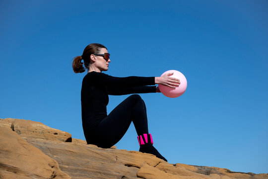 Woman in Black Sportswear Holding Pink Pilates Ball on Rocks