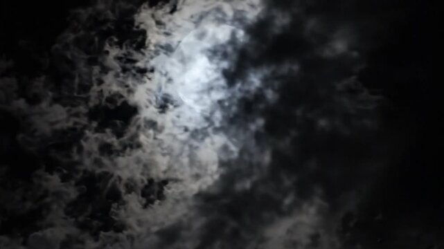 Full moon shines brightly in the night sky with clouds surrounding it