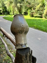 Obraz premium Old clay pot displayed on a rustic wooden post beside a green path in a peaceful summer park