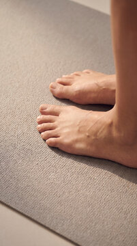 Close-up of bare feet standing on a gray exercise mat in a sunlit studio