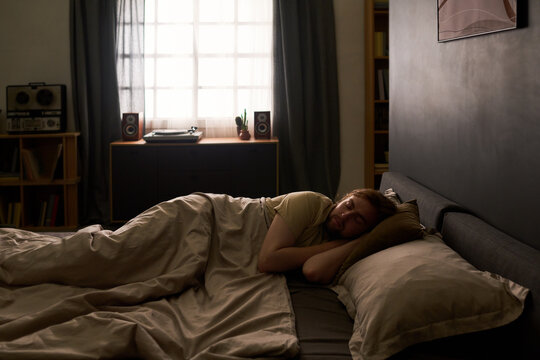 Young adult Caucasian man sleeping in bed resting during morning routine. Visual concept suitable for sleep health, wellness campaigns and insomnia treatment marketing