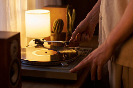 Young adult Caucasian man placing stylus needle on vinyl record turntable at home. Closeup suitable for music streaming campaigns and lifestyle marketing