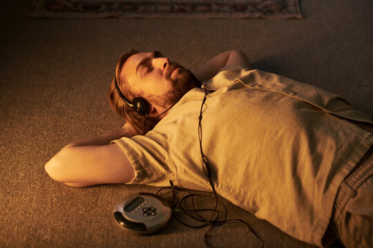 Young adult Caucasian man lying on floor listening to audio with headphones and CD player. Concept representing mental wellbeing, relaxation, leisure time, suitable for lifestyle advertising