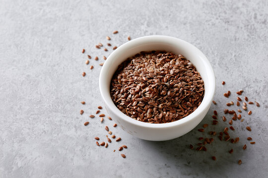 Brown seeds in a white bowl on a gray surface