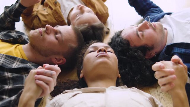 Group of four people lying on the floor holding hands while eyes are closed during a group activity in a light filled room