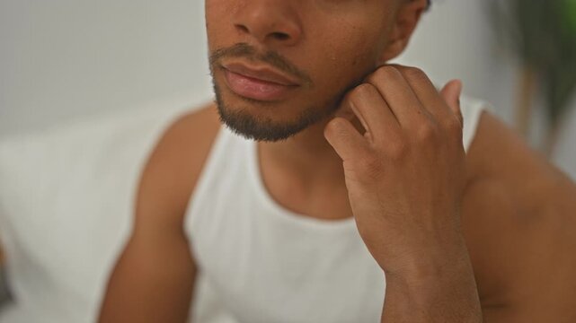 Man touching chin with hand, beard and lips visible, wearing white tank top in studio; introspection thoughtful.