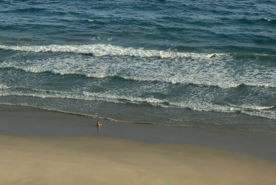 Aerial view of a solo traveller sitting on a white sandy beach in front of breaking waves along the shore of Con Son Island in the Con Dao archipelago during warm sunset light