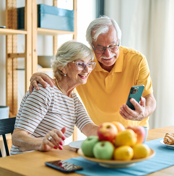 Happy active senior couple having fun using smartphone  during oline video call conversation with family at home