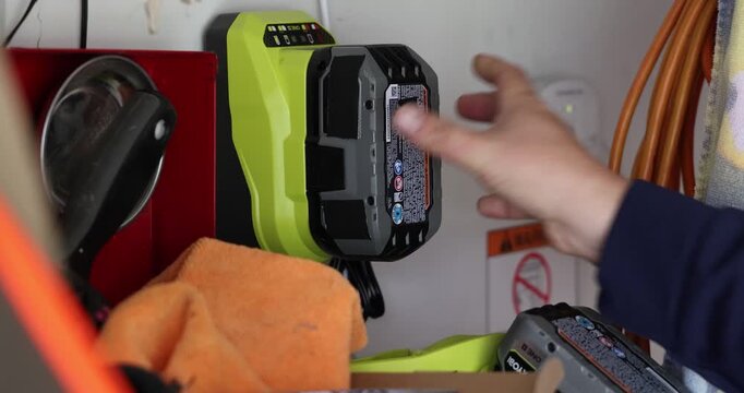 Power Tool Battery Charging Process, A person inserts a lithium ion battery pack into a wall mounted charger in a workshop setting to replenish power for cordless construction equipment