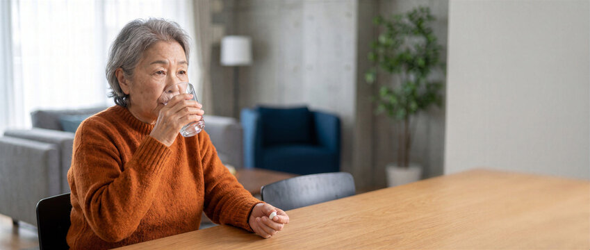 Asian senior woman taking vitamin supplement with water