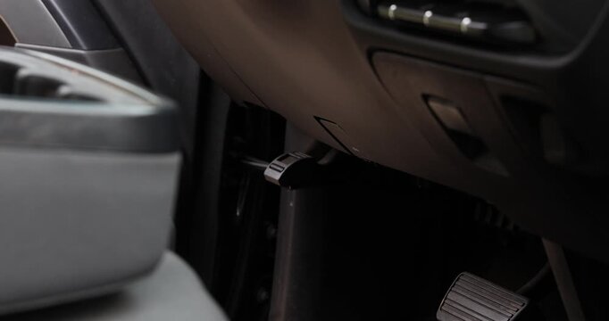 Car Hood Release Lever Operation, A close up view shows a hand pulling the interior hood release lever located under the dashboard of a modern vehicle to open the engine compartment