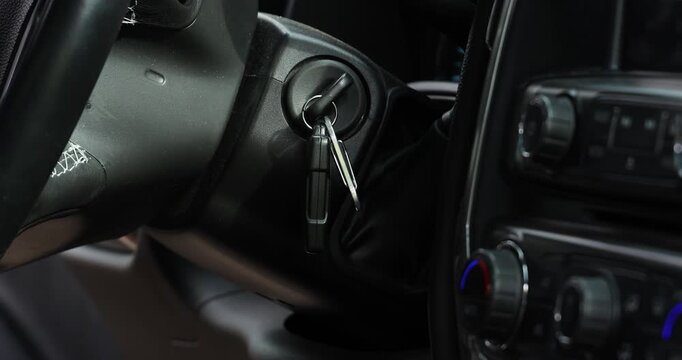 Driver Starting Vehicle Engine, A close up view of a hand inserting and turning a metal key in the ignition switch to activate the engine of a modern pickup truck interior