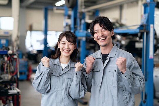 自動車工場で働く若手男女整備士が笑顔でガッツポーズをする職場風景
