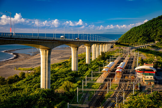 Passenger trains wait below a coastal highway beside the Pacific