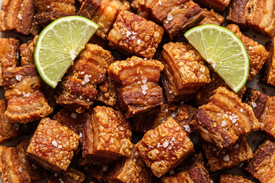 Crispy pork belly cracklings chicharrones with lime wedges, classic Mexican dish