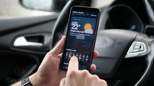Driver compares changing weather forecasts on a smartphone, highlighting mobile climate data, road safety awareness and smarter travel decisions during unstable conditions.
