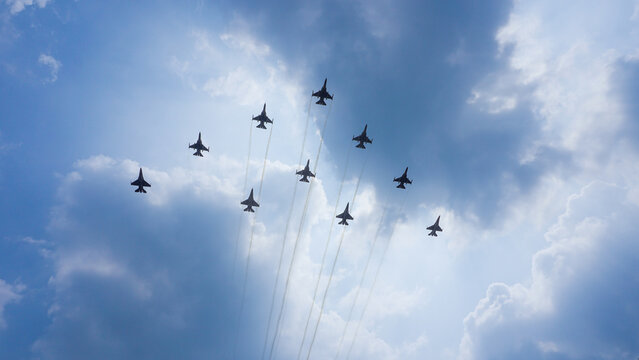 A squadron of military fighter jets flying in formation through a cloudy blue sky leaving smoke trails