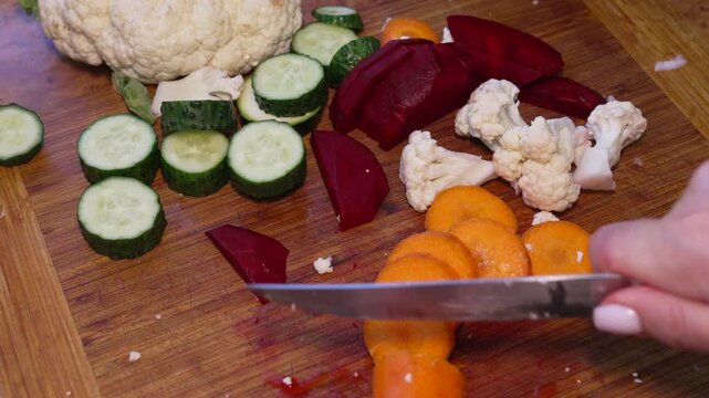 Carrot slicing knife, preparing raw vegetables on wooden board for healthy vegetarian cooking in kitchen, close up view of fresh food preparation
