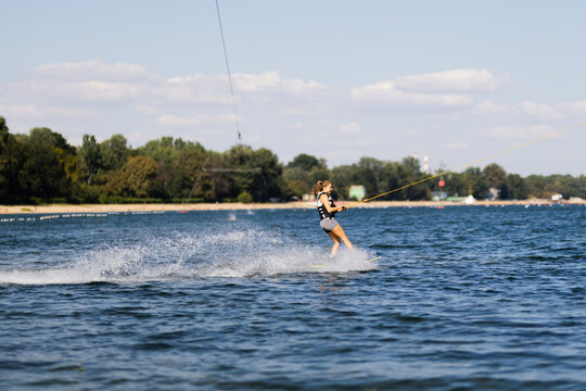 Female wakeboarder wakesurfing. Girl riding waterski cabel. Holding tow rope. Summer activities in the lake.