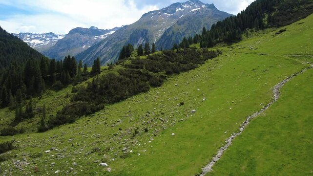 Alpine national park shown in an aerial shot. Alps mountain landscape with green meadows and snow-capped peaks seen in a drone flyover.