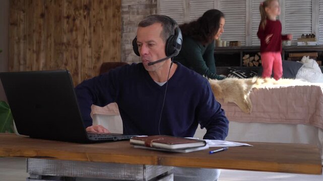 A man works remotely from home. Children play noisily. Tired sad stressed out father