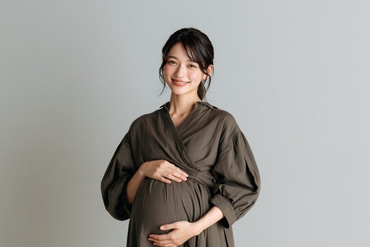 笑顔で大きく膨らんだお腹を優しく抱える日本人妊婦の姿