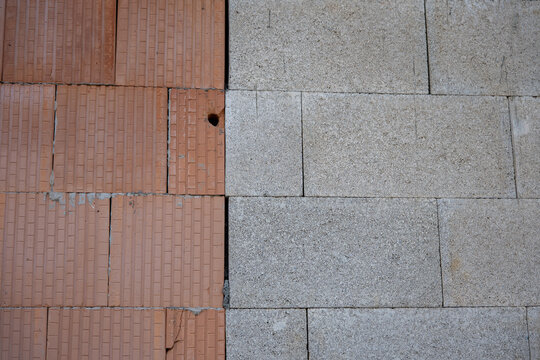 Close-up comparison of red clay bricks and gray concrete blocks in an unfinished masonry wall, showing contrasting building materials, textures and wall construction techniques.