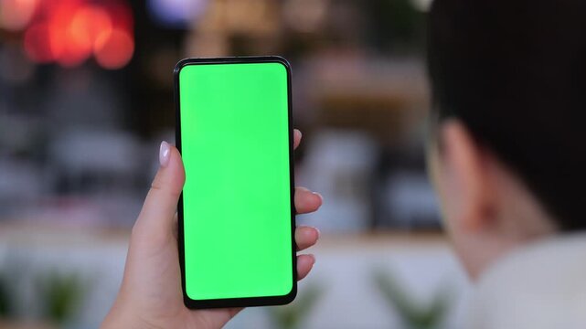 Person holds phone with green screen. Background is blurred cafe setting. Three keyframes show same scene