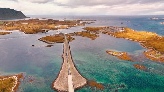 Aerial drone shot pulling back and tilting up over coastal road and bridge in Norway with scenic archipelago and ocean landscape
