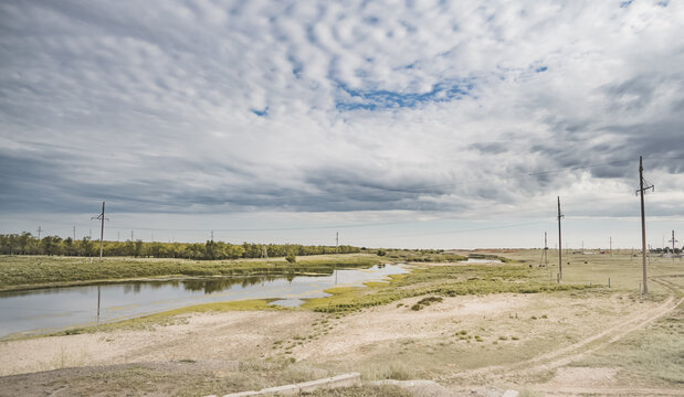 Steppe river flowing through the wild steppes of Kazakhstan in summer under cloudy skies; steppe landscape for background