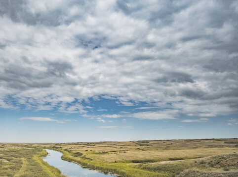 Steppe river flowing through the wild steppes of Kazakhstan in summer under cloudy skies; steppe landscape for background
