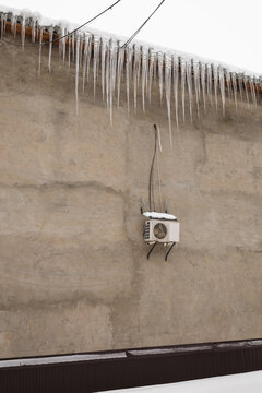 Icicles hanging from the roof along a concrete wall with an air conditioner, winter danger and safety risk