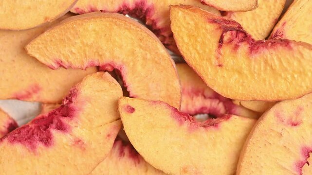 Rotating freeze-dried peach pieces filmed in top-down macro close-up under bright studio lighting. Dehydrated orange and pink fruit texture fills the full frame.