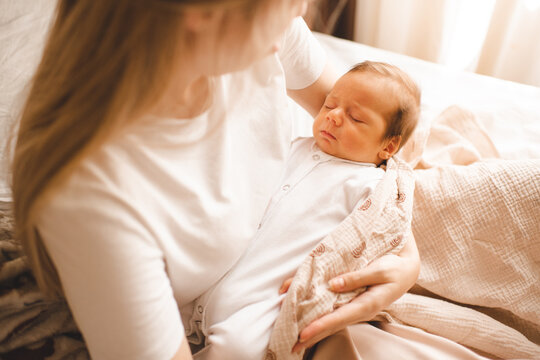 Frowning sad baby boy sleeping on mothers hands with colic pain in bed close up. Motherhood.
