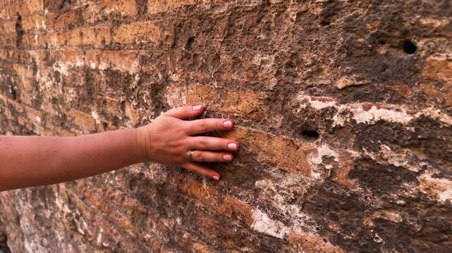 Hand touching ancient stone wall texture, historical brick architecture close-up.