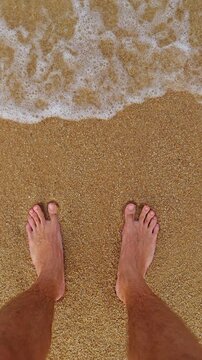 Two Bare Feet Stand While Gentle Waves Wash Over Golden Sand at a Beach, First Person Top Down View Suggesting Summer Relaxation and Travel Vertical video.
