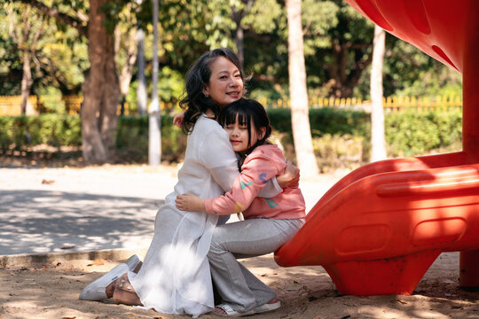 Asian Older Woman Embracing Young Girl on Playground Slide: Fami