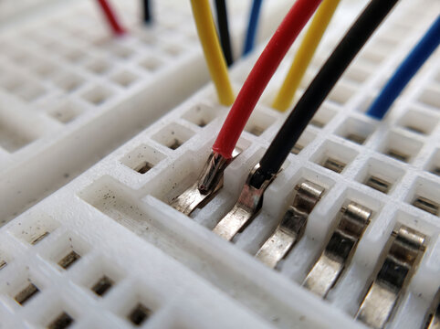 Detailed macro view of jumper wires plugged into white solderless breadboard terminal.