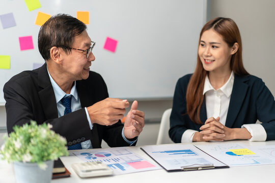 A man and a woman are sitting at a table with a whiteboard behind them