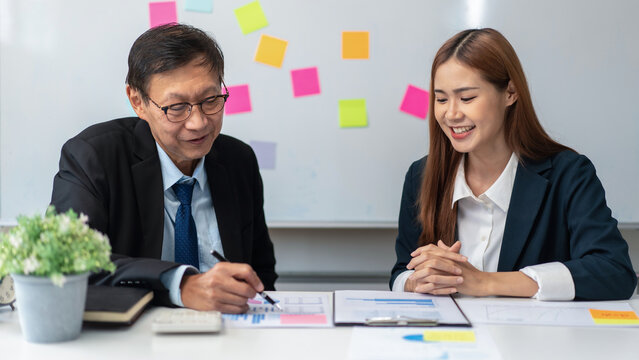Two people in suits are sitting at a table with a white board behind them