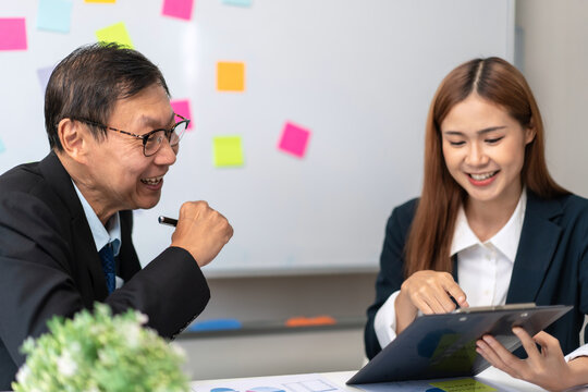 A man and a woman are sitting at a table with a white board behind them