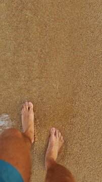Bare Feet Walk Through Shallow Seawater on Golden Sand in a First Person Downward View, Showing Summer Leisure and Coastal Lifestyle Vertical video.