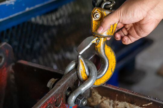 A mechanic connects a yellow crane hook to a metal shackle.