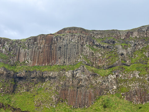 Extensive basalt columns form dramatic layered cliffs amid green slopes near Giant&rsquo;s Causeway on the Causeway Coast of County Antrim, Northern Ireland.