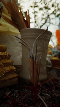Burning Incense Sticks Stand in Ash Before Ceramic and Golden Shrine Objects, Showing Spiritual Ritual and Devotion Vertical video.