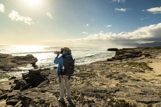 female photographer overlooking elevated view of massive wave sets rolling into Walker Bay Nature Reserve, South Africa 