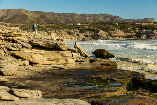 female photographer overlooking elevated view of massive wave sets rolling into Walker Bay Nature Reserve, South Africa 