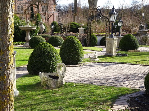 Barocker Schlossgarten mit Formschnitt-Buchsbaum, antiken Statuen und Springbrunnen an einem sonnigen Tag