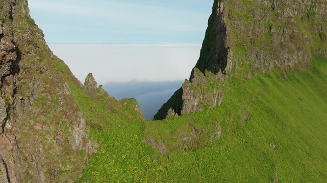 Aerial push in drone shot reveals the dramatic rugged cliffs of K&aacute;lfatindar mountain and a vast sea of clouds on Iceland's remote Westfjords. Hundreds of birds are nesting in the steep walls.