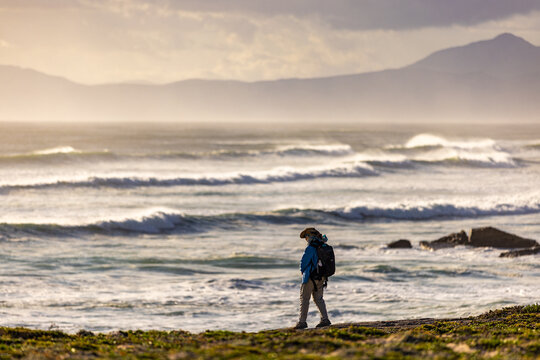 solo female photographer/hiker overlooking cliff with view you massive waves reaching Walker Bay Nature Reserve beach, South Africa at sunset